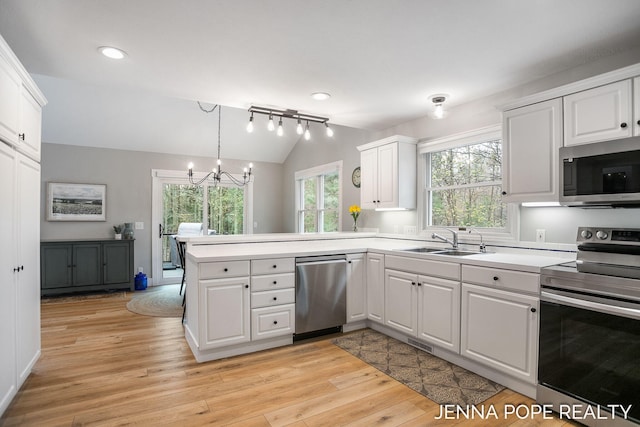 16840 Cricket Ct, Grand Haven, MI 49417 - kitchen featuring appliances with stainless steel finishes, a sink, lofted ceiling, a peninsula, and light wood-style floors