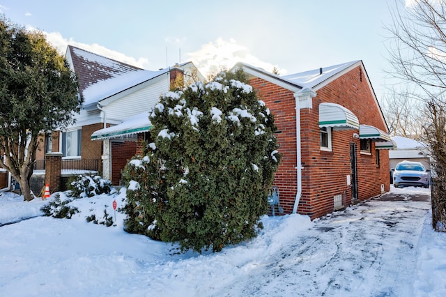 view of snowy exterior featuring brick siding and a garage