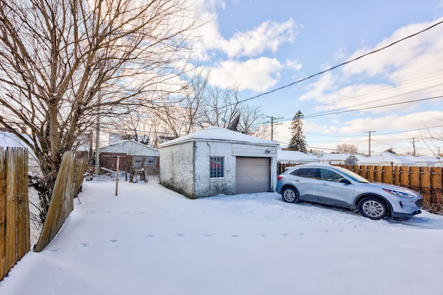 snow covered structure featuring fence, a garage, and an outbuilding