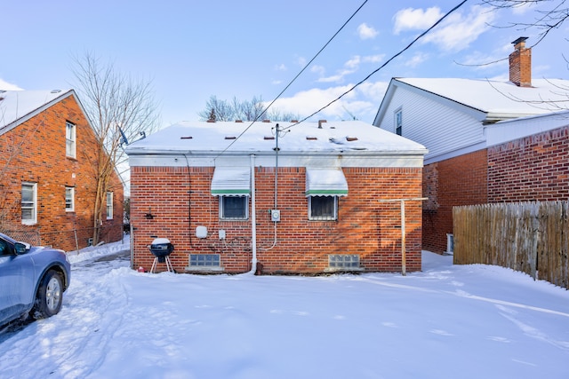 snow covered property featuring fence and brick siding