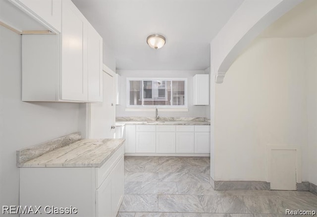 kitchen featuring white cabinetry, light countertops, arched walkways, a sink, and light marble finish floors