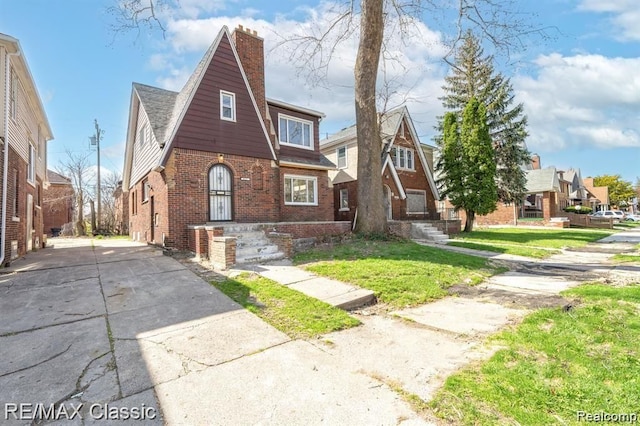 english style home with brick siding, a chimney, a front lawn, and driveway
