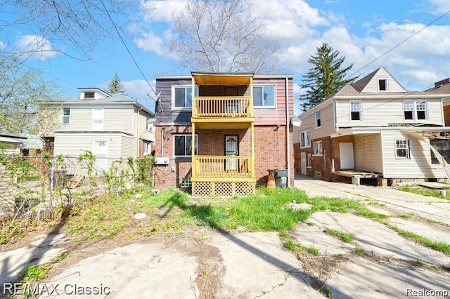 rear view of property with a balcony, brick siding, and fence
