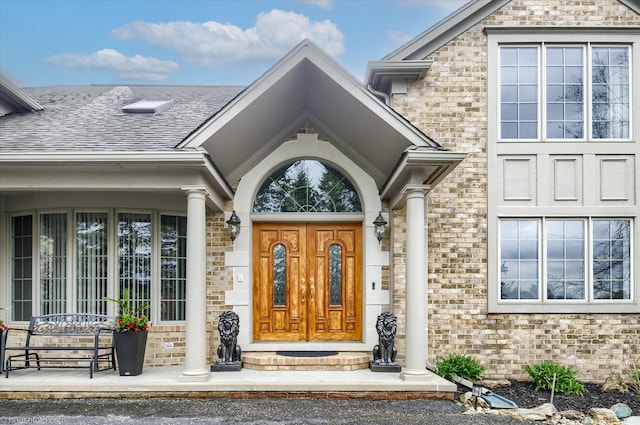 entrance to property featuring brick siding and roof with shingles