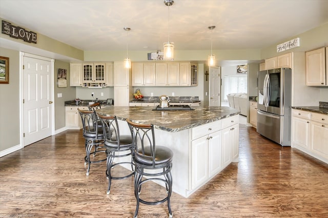 kitchen featuring stainless steel fridge, dark wood-type flooring, a kitchen island, glass insert cabinets, and a breakfast bar area