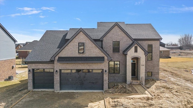french provincial home featuring brick siding, a shingled roof, and dirt driveway