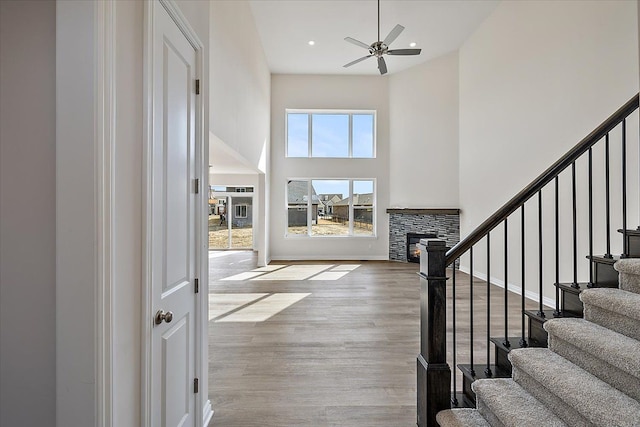 entrance foyer with a high ceiling, ceiling fan, a fireplace, stairway, and wood finished floors