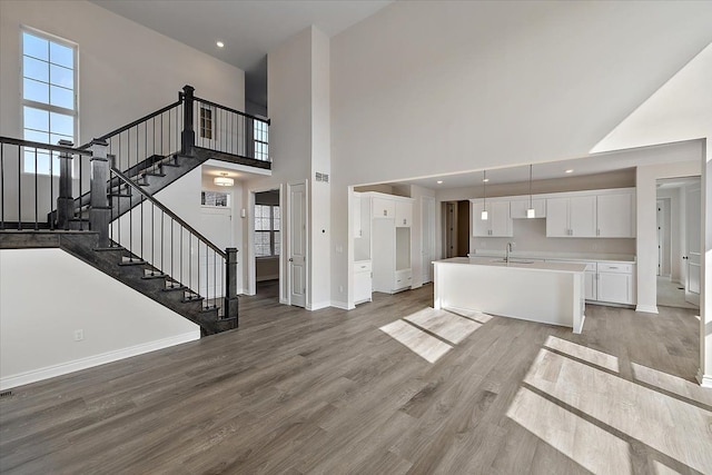 unfurnished living room with a sink, a high ceiling, baseboards, light wood-style flooring, and stairway
