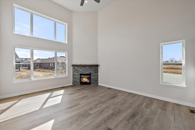 unfurnished living room with a towering ceiling, ceiling fan, wood finished floors, a fireplace, and baseboards