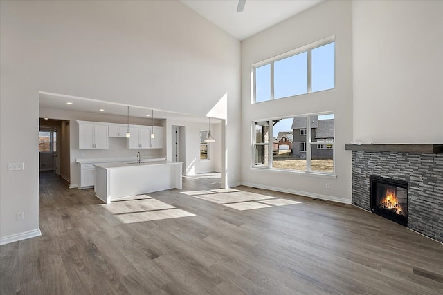 unfurnished living room with high vaulted ceiling, a stone fireplace, a sink, wood finished floors, and baseboards