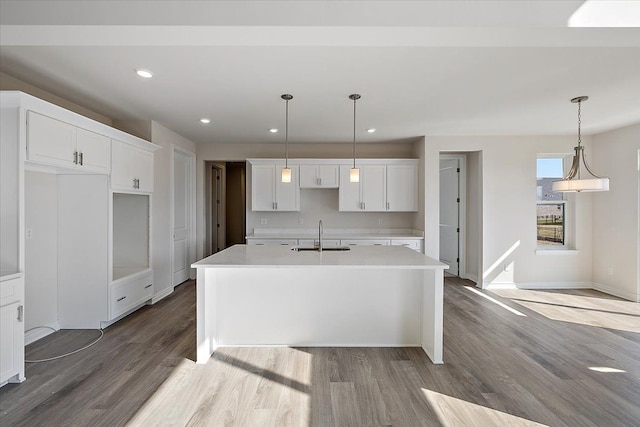 kitchen featuring a sink, wood finished floors, a center island with sink, white cabinetry, and baseboards