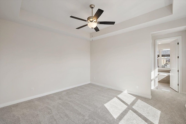 empty room with a raised ceiling, light carpet, and baseboards