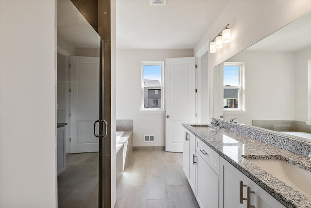 full bath featuring a bath, double vanity, a stall shower, and baseboards