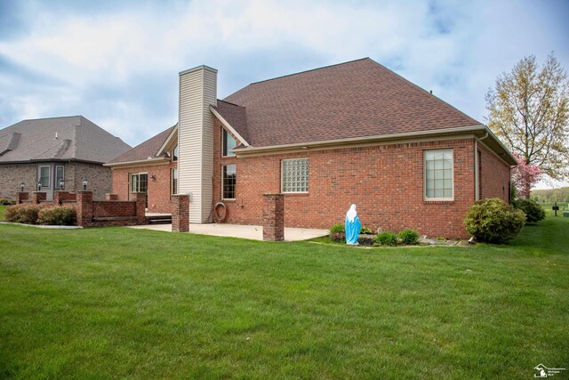rear view of property featuring brick siding, a chimney, a yard, a patio area, and a shingled roof