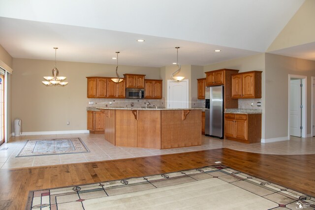 kitchen with stainless steel appliances, brown cabinetry, light wood-style flooring, a kitchen bar, and recessed lighting