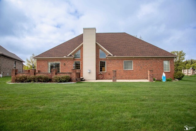 rear view of house featuring brick siding, a chimney, a yard, and roof with shingles
