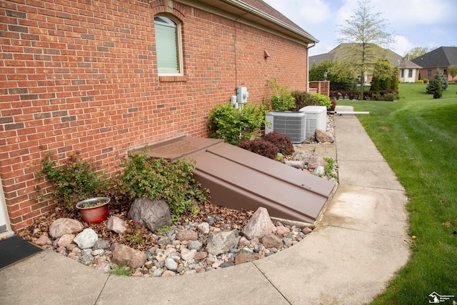 view of property exterior with central air condition unit, a lawn, and brick siding