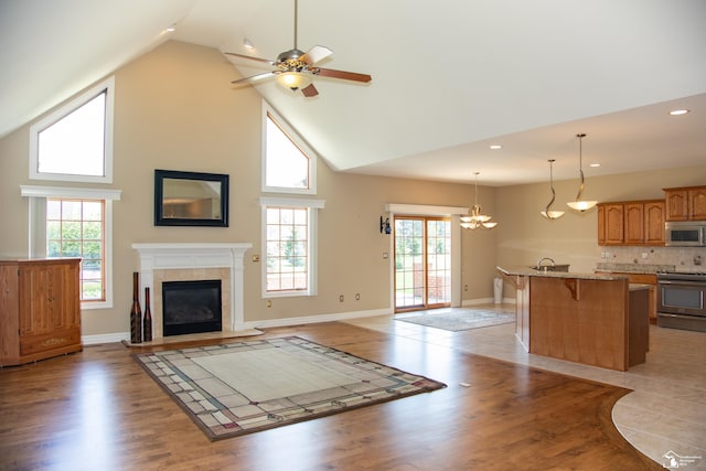 unfurnished living room with high vaulted ceiling, a ceiling fan, a tile fireplace, plenty of natural light, and light wood-type flooring