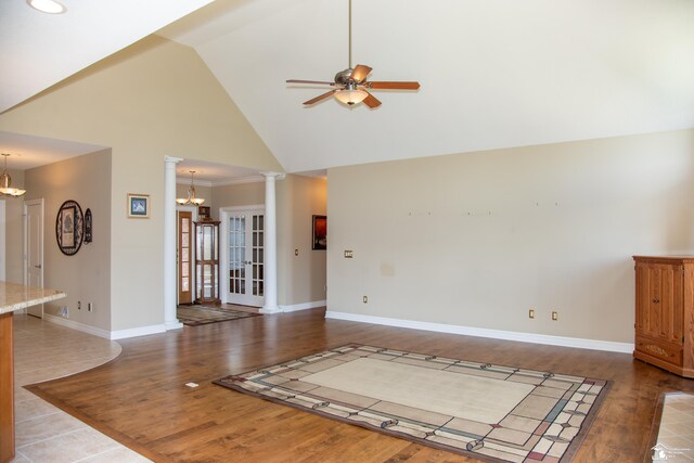 unfurnished living room with a ceiling fan, a chandelier, high vaulted ceiling, wood finished floors, and baseboards