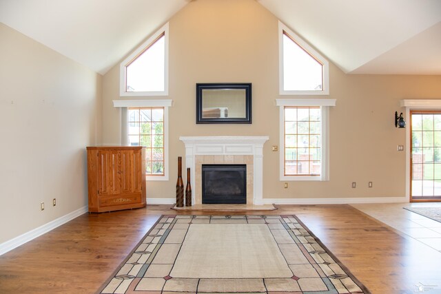 unfurnished living room featuring light wood-style floors, high vaulted ceiling, a tiled fireplace, and baseboards