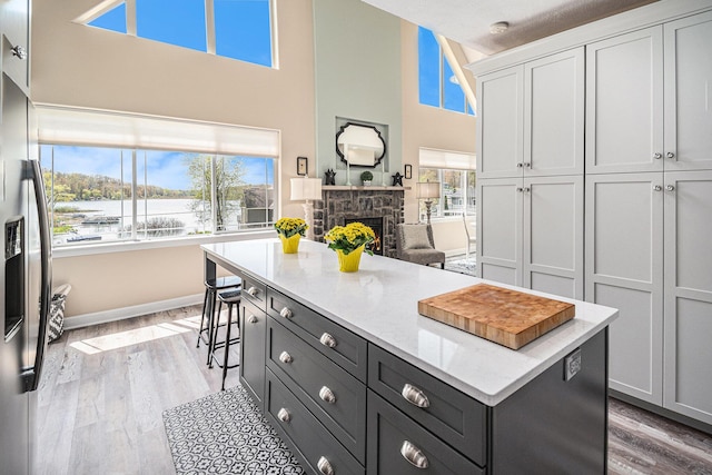 7379 Wimpole Dr NE, Belding, MI 48809 - kitchen featuring light wood-style floors, stainless steel refrigerator with ice dispenser, a stone fireplace, white cabinetry, and a kitchen island