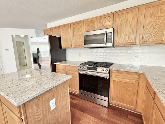 kitchen featuring appliances with stainless steel finishes, hardwood / wood-style flooring, decorative backsplash, light stone countertops, and a textured ceiling