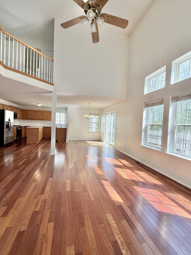 unfurnished living room featuring a towering ceiling, dark wood-style floors, healthy amount of natural light, and a ceiling fan