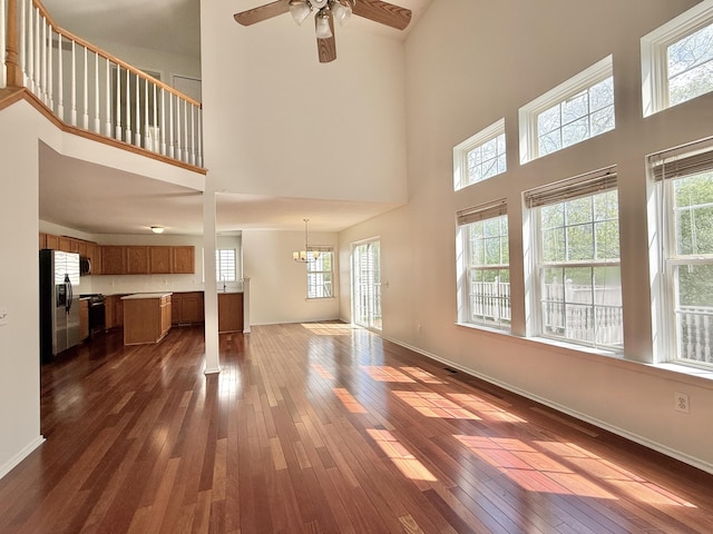 unfurnished living room with plenty of natural light, a towering ceiling, dark wood-style floors, ceiling fan, and baseboards