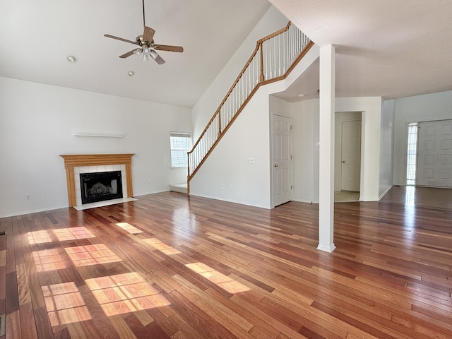 unfurnished living room with stairs, a ceiling fan, light wood finished floors, a tile fireplace, and high vaulted ceiling