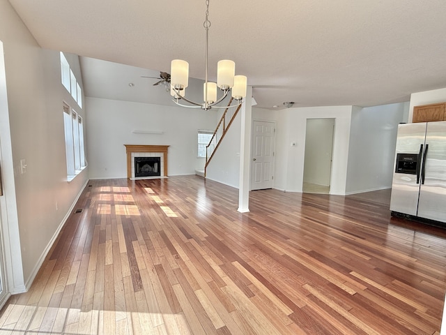 unfurnished living room with light wood finished floors, a tile fireplace, a chandelier, stairway, and baseboards