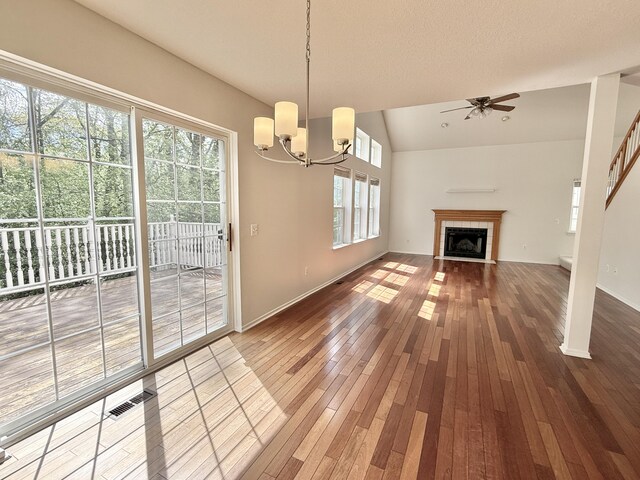 unfurnished dining area featuring hardwood / wood-style floors, ceiling fan, a chandelier, lofted ceiling, and a fireplace