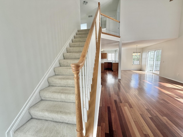 stairs featuring hardwood / wood-style flooring, a towering ceiling, baseboards, and a chandelier