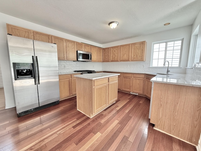 kitchen with stainless steel appliances, a sink, wood-type flooring, tasteful backsplash, and a textured ceiling