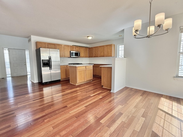 kitchen featuring stainless steel appliances, a chandelier, hardwood / wood-style floors, light countertops, and a center island