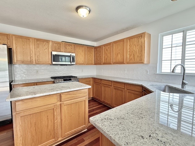 kitchen with stainless steel appliances, a sink, dark wood finished floors, light stone countertops, and decorative backsplash