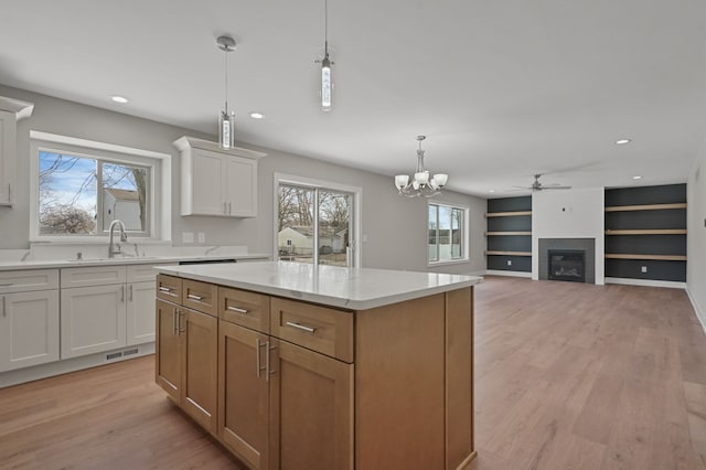 53302 Zachary Dr, Chesterfield, MI 48047 - kitchen featuring light wood-type flooring, a glass covered fireplace, decorative light fixtures, a sink, and white cabinets
