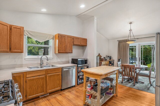 kitchen with appliances with stainless steel finishes, vaulted ceiling, a sink, light wood-style floors, and light countertops