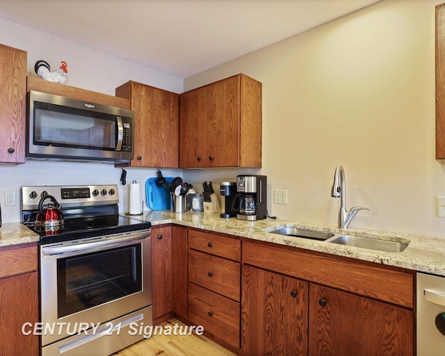 730 S Point Rd, Gladwin, MI 48624 - kitchen with appliances with stainless steel finishes, a sink, brown cabinetry, light stone counters, and light wood-style floors