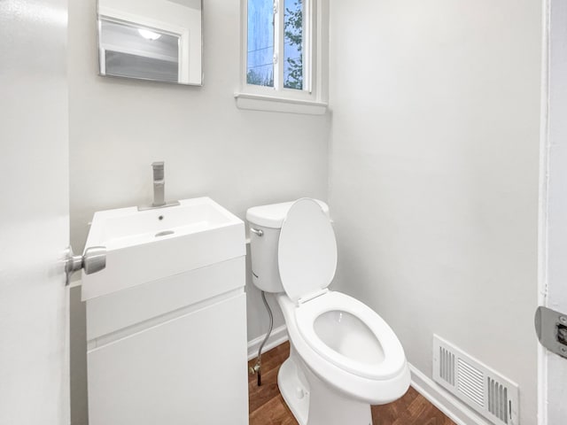 half bath with vanity, toilet, baseboards, and wood finished floors