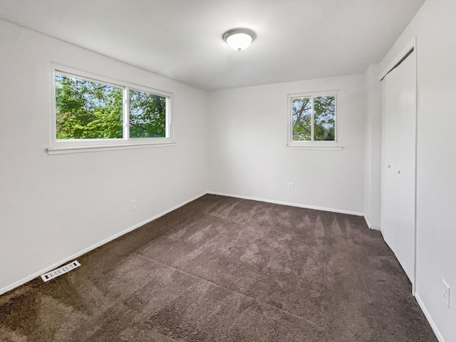 unfurnished bedroom with dark carpet, baseboards, and a closet