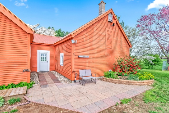 exterior space featuring a patio, metal roof, a chimney, and a lawn