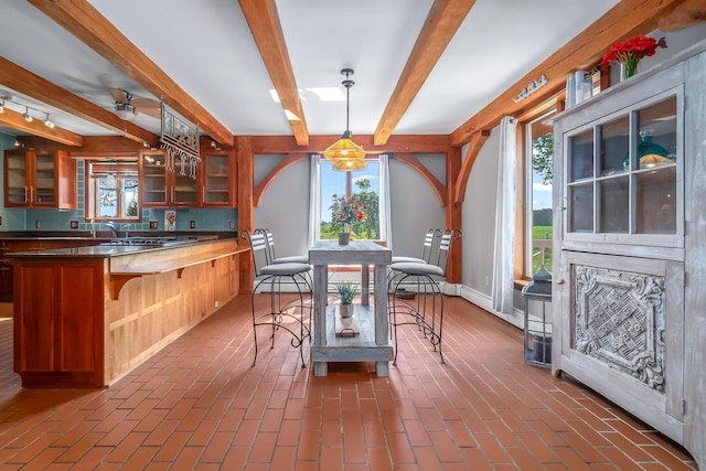 dining space featuring healthy amount of natural light, beam ceiling, brick floors, and baseboards
