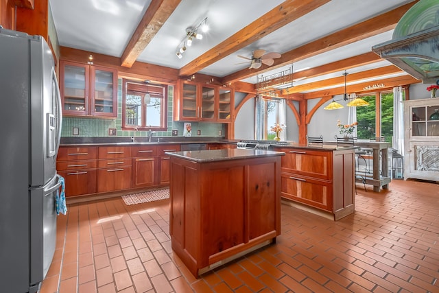 kitchen featuring stainless steel refrigerator with ice dispenser, a center island, tasteful backsplash, brown cabinets, and brick floors