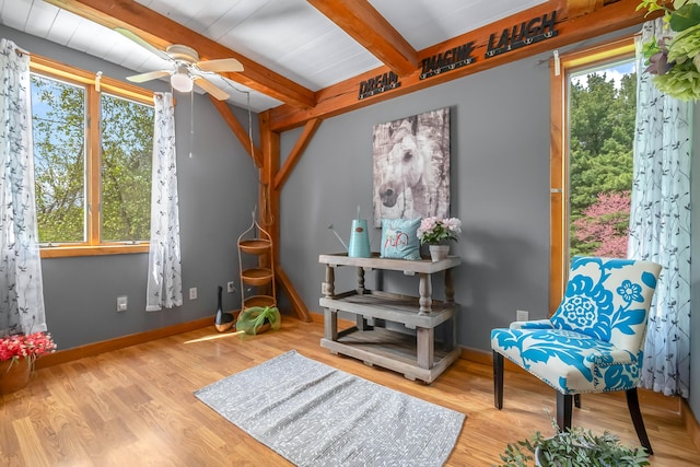 living area with plenty of natural light, ceiling fan, beamed ceiling, wood finished floors, and baseboards