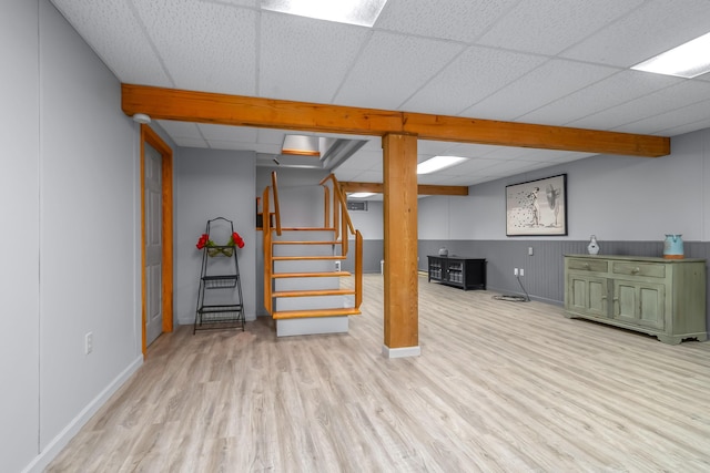 finished below grade area featuring wood finished floors, a drop ceiling, baseboards, and stairs