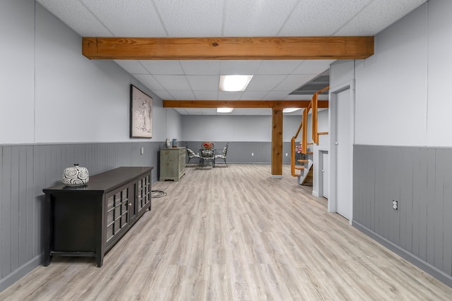 finished below grade area with light wood-type flooring, wainscoting, stairs, and a drop ceiling