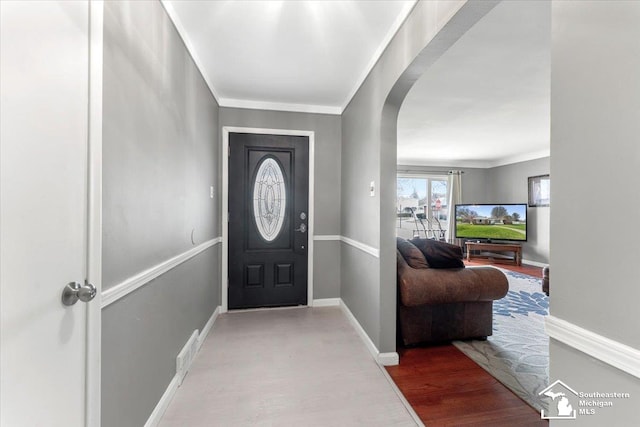 entryway featuring arched walkways, baseboards, wood finished floors, and ornamental molding