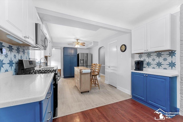 kitchen with stainless steel appliances, blue cabinets, light wood-style floors, light countertops, and decorative backsplash