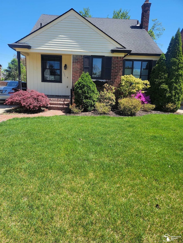 view of front of house with a front yard, a chimney, covered porch, and a shingled roof