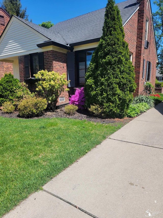 view of front of home with brick siding, a front yard, a chimney, and a shingled roof
